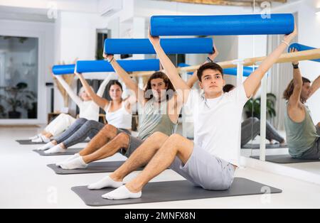 Men and women practicing pilates with roller on gray mat in gym room Stock Photo