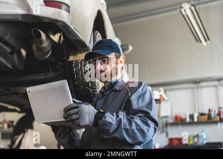 Skilled car mechanic using a computer to diagnose and fix the white car on lift. High-quality photo Stock Photo