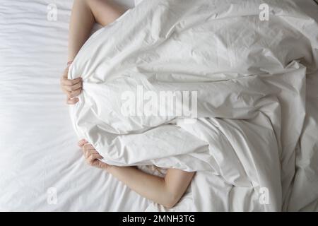 Girl lying in bed covering her face with blanket Stock Photo
