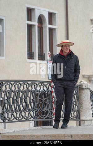 A gondolier in a traditional straw hat stands on a bridge in Venice waiting for customers. Gondolas are a major touristic transport in Venice, Italy Stock Photo