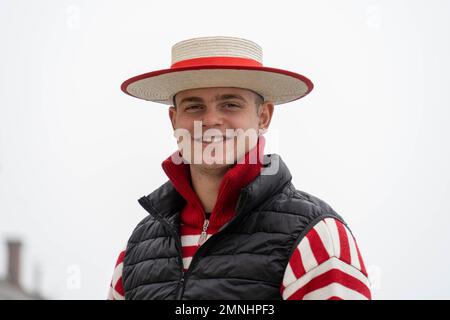 A gondolier in a traditional straw hat stands on a bridge in Venice waiting for customers. Gondolas are a major touristic transport in Venice, Italy Stock Photo