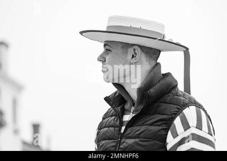 A gondolier in a traditional straw hat stands on a bridge in Venice waiting for customers. Gondolas are a major touristic transport in Venice, Italy Stock Photo