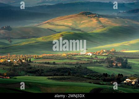 Rolling green hills and fields with early morning sun lighting the tops of the hills near Volterra, Tuscany, Italy Stock Photo