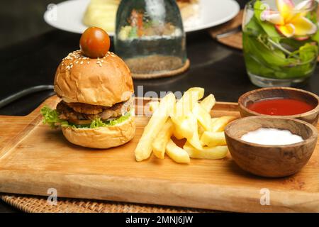Small size burger served with french fries and sauces on the wooden board in cafe Stock Photo