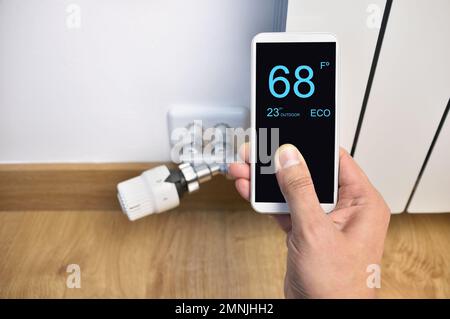 close up of a person hand adjusting temperature on thermostat through smart phone at home Stock Photo