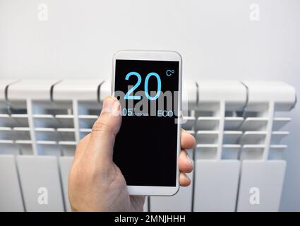 close up of a person hand adjusting temperature on thermostat through smart phone at home Stock Photo