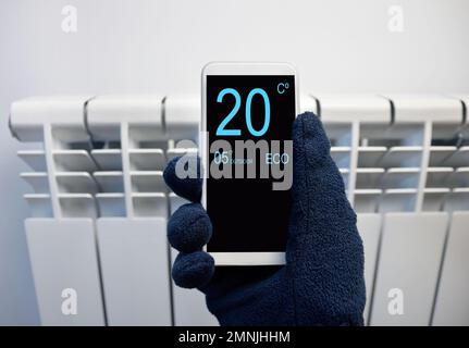 close up of a person hand adjusting temperature on thermostat through smart phone at home Stock Photo