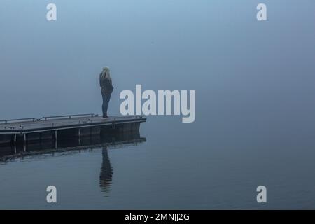 Senior woman standing on jetty in foggy morning Stock Photo