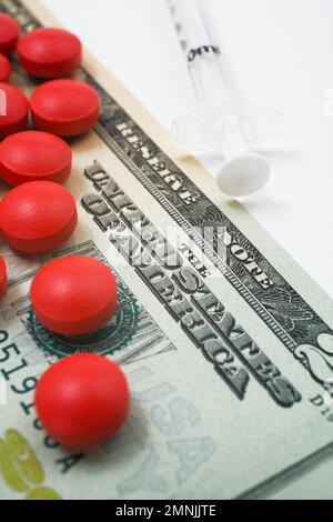 Red medicine pills on top of US twenty dollar bill next to syringe. Stock Photo