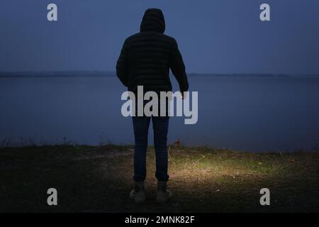 Man with flashlight walking near river in evening Stock Photo