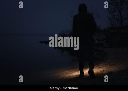 Man with flashlight walking near river in evening Stock Photo