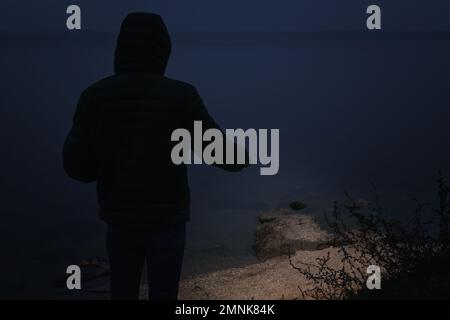 Man with flashlight walking near river in evening Stock Photo
