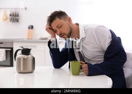 Sleepy man with cup of drink at home in morning Stock Photo