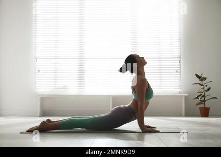 Side view of woman doing core stretch on fitness mat. Young female