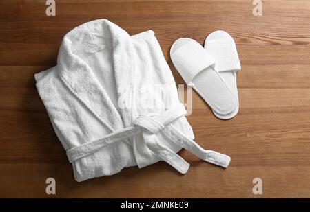 Clean folded bathrobe and slippers on wooden background, flat lay Stock Photo