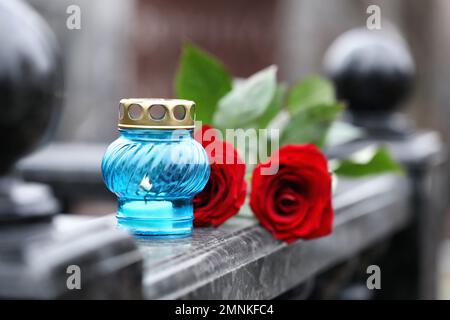 Red roses and candle on black marble tombstone outdoors. Funeral ceremony Stock Photo