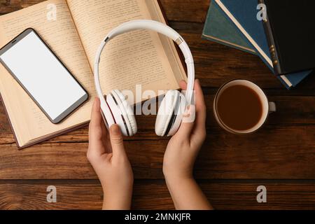 Woman holding headphones over wooden table with books, top view Stock Photo