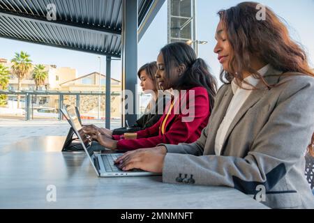 Three businesswomen work by typing on their digital devices. Copy space on the left Stock Photo