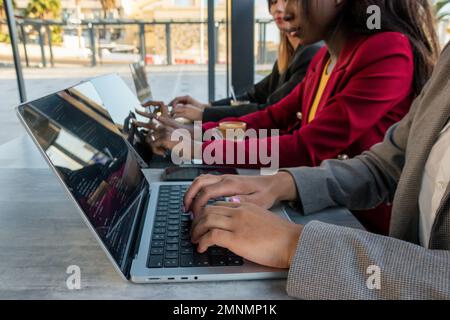 Close-up of the hands of three female programmers typing some code with their digital devices Stock Photo