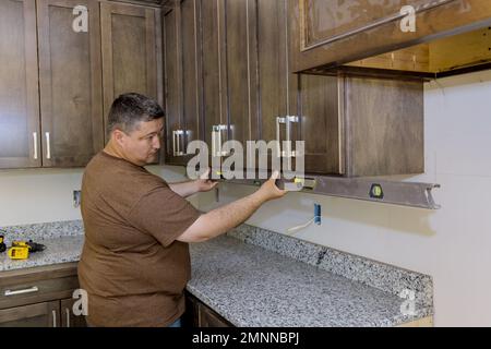 Installing new kitchen cabinets furniture set by worker who is using level for leveling Stock Photo