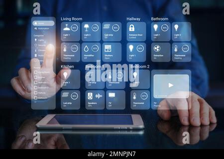 Person using smart home dashboard interface to control connected devices and set up automations. Futuristic virtual screen HUD above digital tablet co Stock Photo