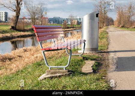 Zurich, Switzerland, January 19, 2023 A red empty bench next to a small river on a sunny day just at the international airport Stock Photo