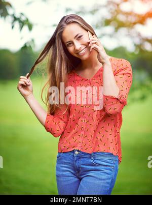 When someone you miss randomly calls or texts you...a young woman twirling her hair while talking on her cellphone outside. Stock Photo