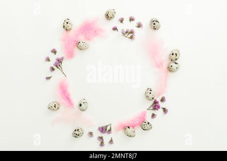 Round composition with easter eggs, flowers and pink feathers on white background. Flat lay, top view Stock Photo