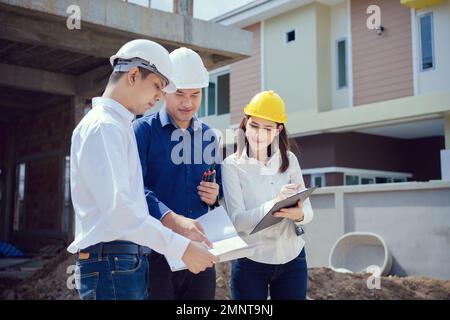 Asian Architector and engineers team with draft plan of building and tablet talking constructing site. Construction manager and engineer working on bu Stock Photo