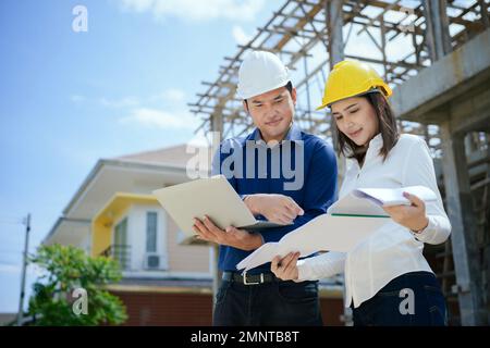 Asian Architector and engineers team with draft plan of building and tablet talking constructing site. Construction manager and engineer working on bu Stock Photo