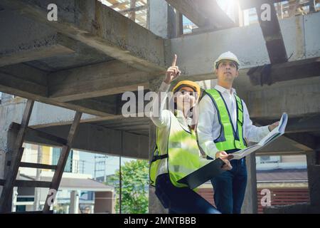 Asian Architector and engineers team with draft plan of building and tablet talking constructing site. Construction manager and engineer working on bu Stock Photo