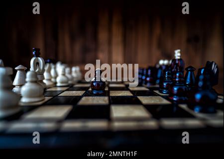 Blurred background with a low depth of focus. The set of wooden chess pieces elements standing on chess board on dark background. Leadership, teamwork Stock Photo
