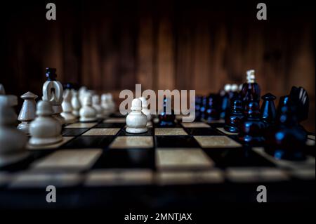 Blurred background with a low depth of focus. The set of wooden chess pieces elements standing on chess board on dark background. Leadership, teamwork Stock Photo