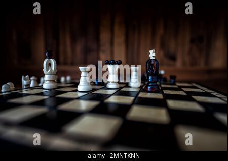 Blurred background with a low depth of focus. The set of wooden chess pieces elements standing on chess board on dark background. Leadership, teamwork Stock Photo