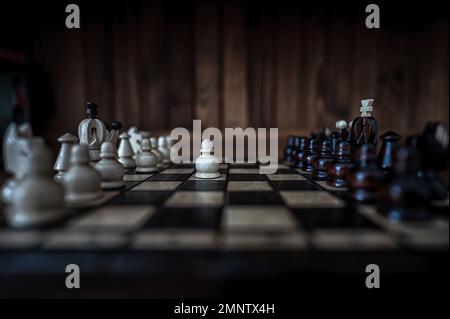 Blurred background with a low depth of focus. The set of wooden chess pieces elements standing on chess board on dark background. Leadership, teamwork Stock Photo