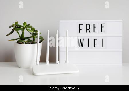 White router, plant and lightbox with free wifi text on table Stock Photo