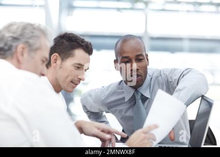 Going over the tax figures. Three businessmen looking over documents while sitting down in a meeting. Stock Photo