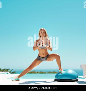 Commitment is the key. an attractive young woman in workout gear working on her fitness by the pool on a sunny day. Stock Photo