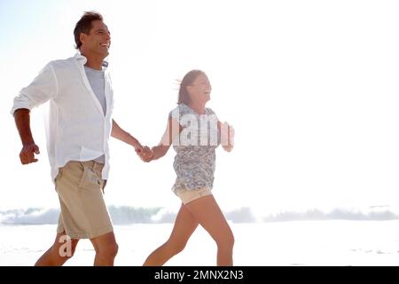 Being on the beach is invigorating. A happy mature couple holding hands while running on the beach. Stock Photo
