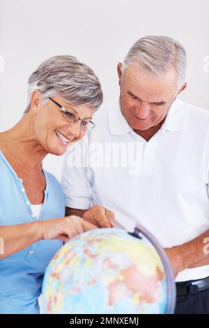 Couple searching travel destination on globe. Happy mature couple planning vacation while looking at globe. Stock Photo