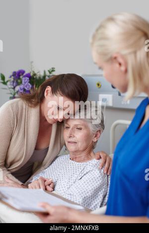 Youll be okay. A daughter consoling her mother in the hospital as a young nurse looks on. Stock Photo