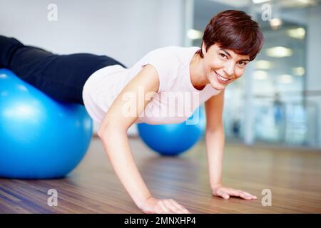 Woman doing push ups on pilates ball. Portrait of woman doing push ups on pilates ball and smiling. Stock Photo