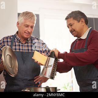 The secret ingredient is always cheese. two senior men cooking in the kitchen. Stock Photo