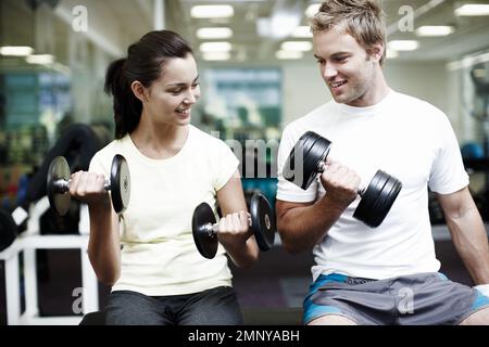 How you doing with that. two people working out using dumbbells in the gym. Stock Photo