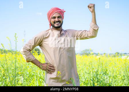 Happy famer showing stroing gesture while standing at farmland by looking at camera - conept of confident, agro business and positive emotion Stock Photo