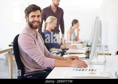 Tackling his work with a can-do attitude. A designer working at his desk with his colleagues in the background. Stock Photo