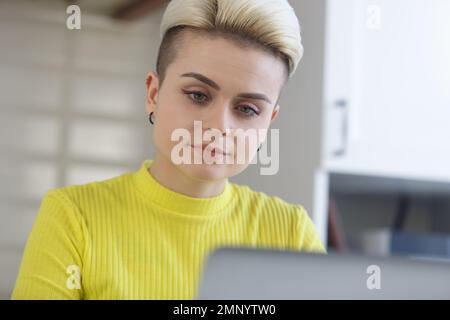 Portrait of female programmer coding on computer at home. Young woman with short hair works freelance with a laptop Stock Photo