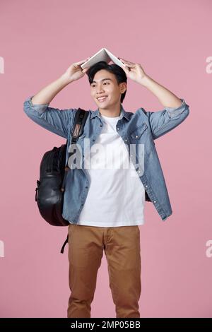 Young male student with open book on his head having fun isolated on a pink background Stock Photo