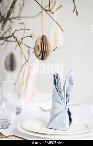 Easter tablescaping with bunny ear napkins and paper eggs hanging on branches. Stock Photo