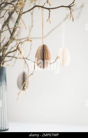 Easter paper eggs hanging on branches against white wall. Stock Photo
